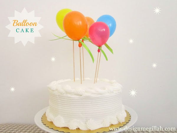 A birthday cake with tiny balloons on skewers sticking out of it