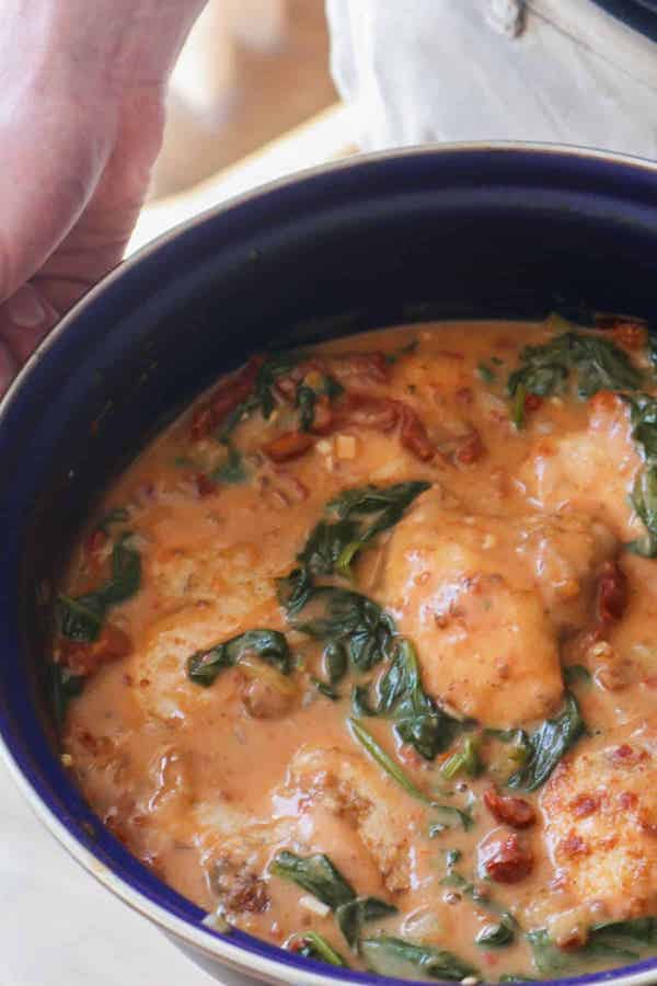 Perosn holding a pot with Tuscan chicken with sundried tomatoes and spinach