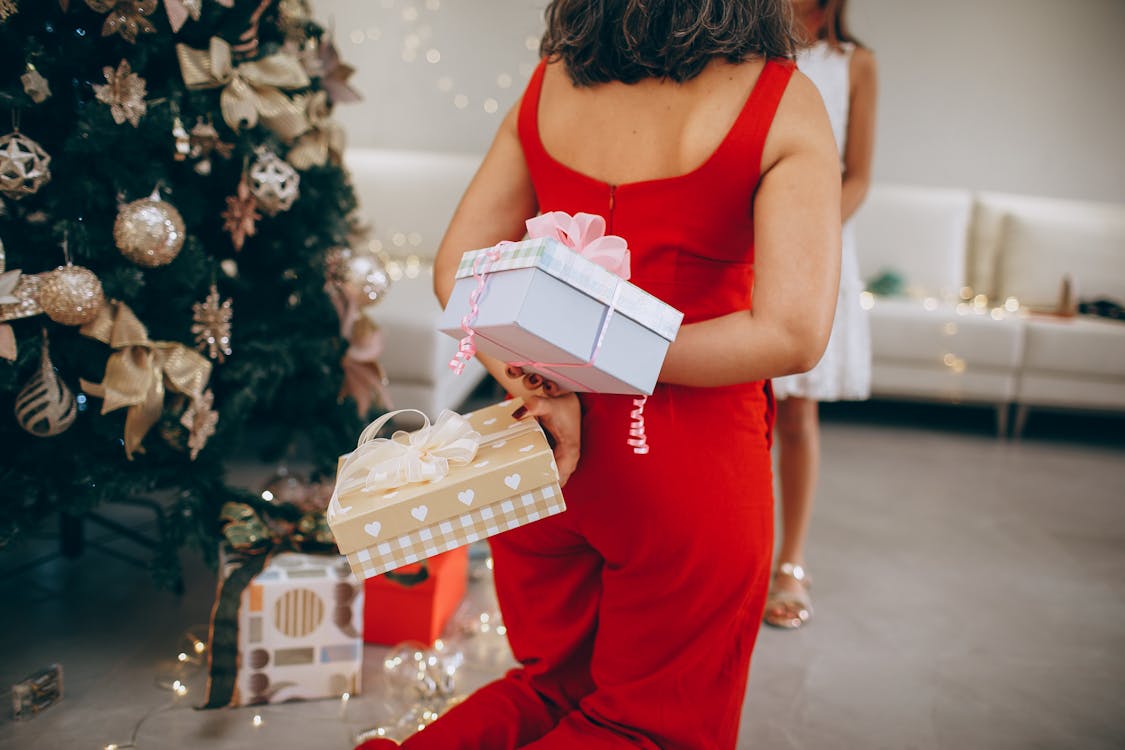 Free Woman in red dress holding Christmas gifts by a decorated tree indoors. Stock Photo