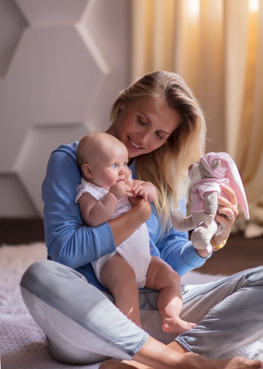 Free Caucasian mother and baby sharing a joyful moment indoors with a plush toy. Warm and loving atmosphere. Stock Photo