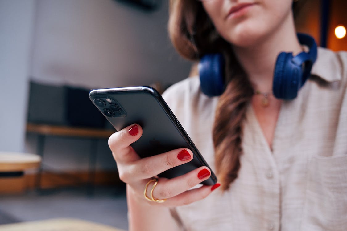 Free Close-up of woman holding smartphone, wearing headphones indoors. Stock Photo