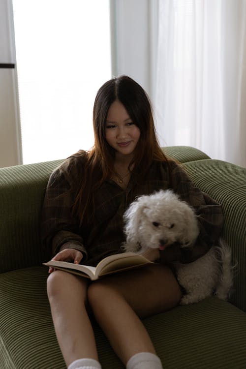 Free Young Brunette with Dog and Book on Sofa Stock Photo