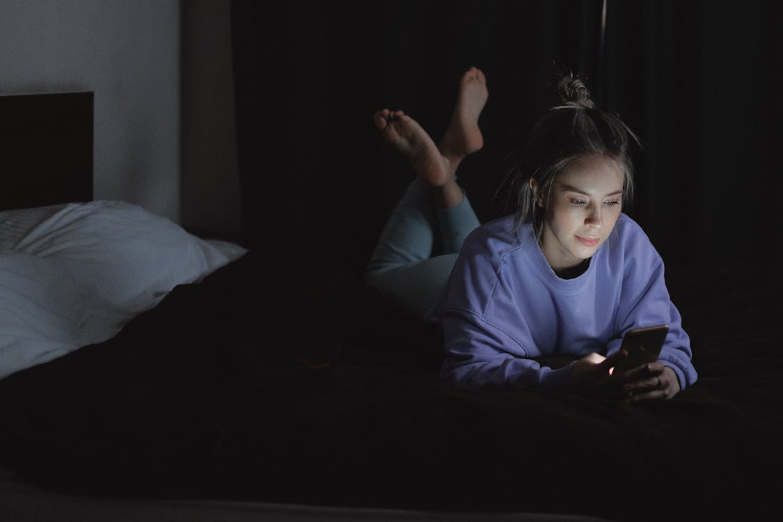 Free Woman Lying on Bed while Using a Cellphone Stock Photo