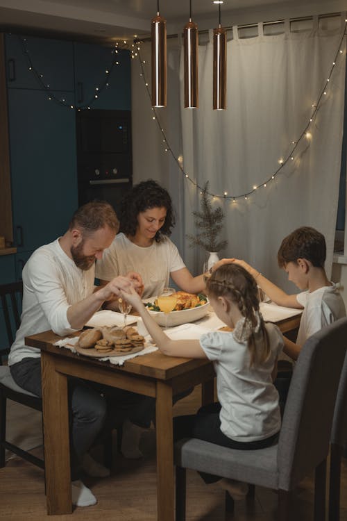 Free A family holding hands and praying around a festive dinner table set with food and decorations. Stock Photo