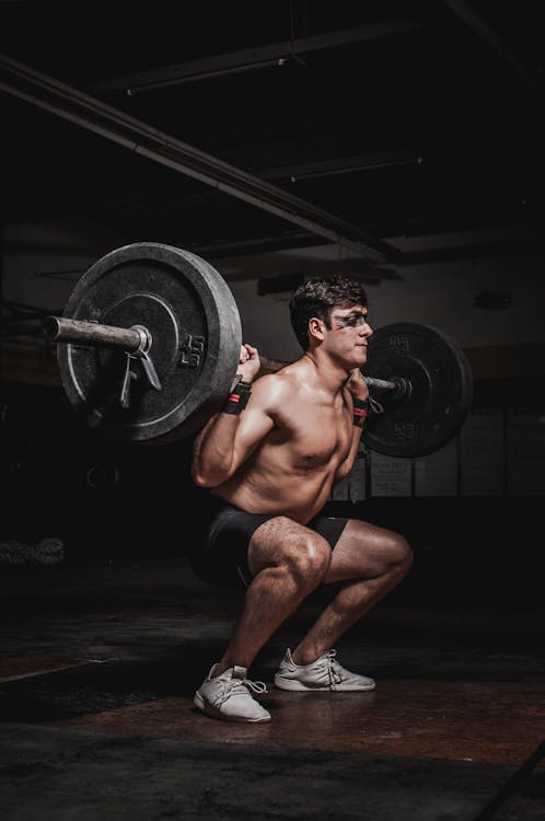 Free Shirtless man performing a barbell squat, showcasing strength and fitness. Stock Photo