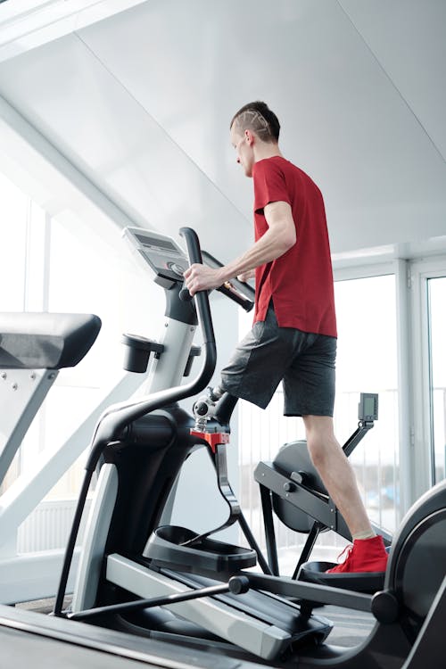 Free Man using an elliptical trainer in a gym wearing a prosthetic leg. Indoor fitness and health focus. Stock Photo