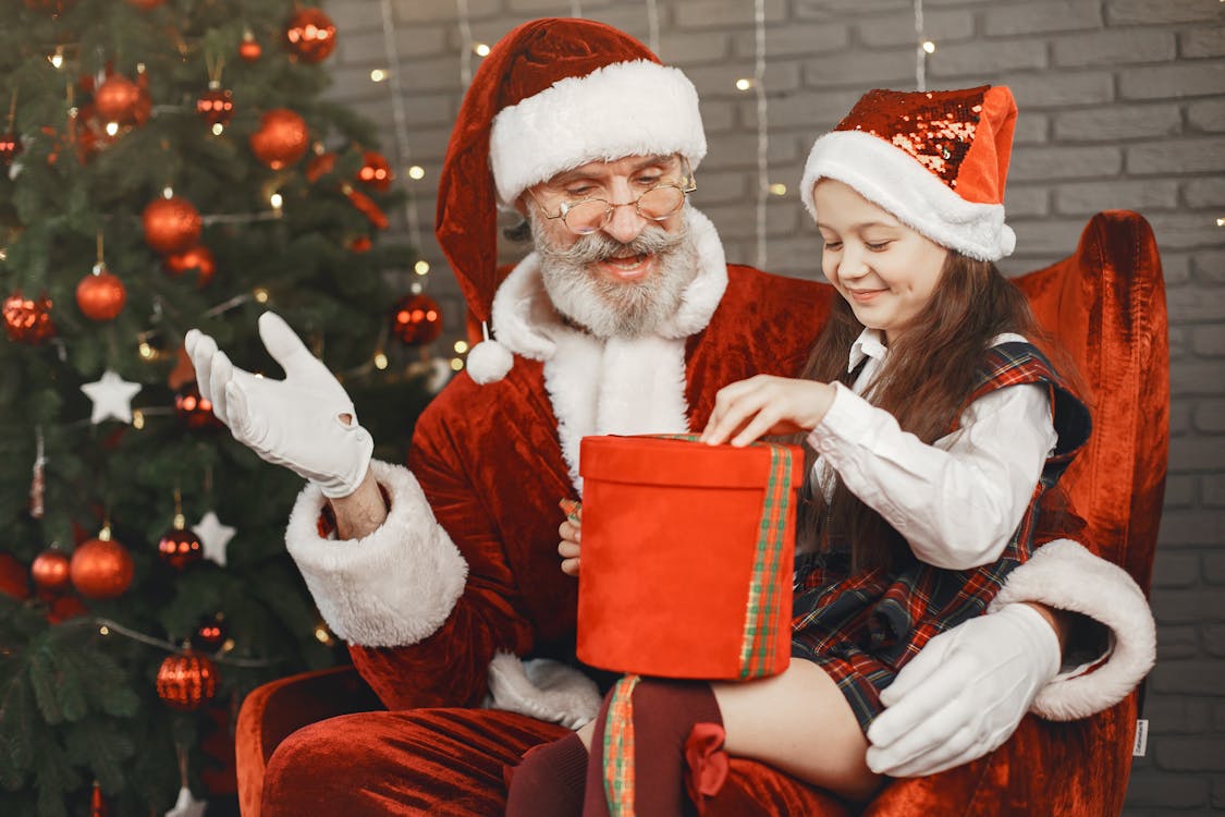 Free A cheerful Santa Claus shares a gift with a delighted child in a festive setting. Stock Photo