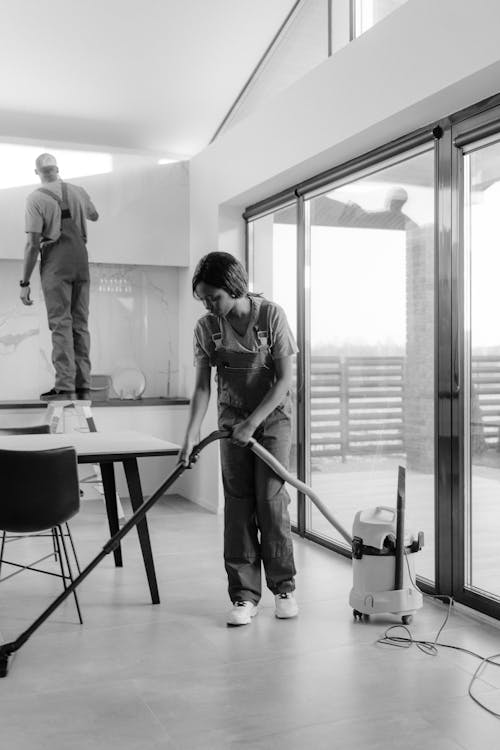 Free Two professional cleaners working in a modern home interior, focusing on vacuuming and dusting. Stock Photo