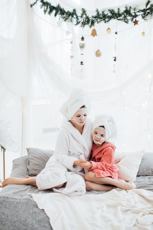 Free Mother and daughter in bathrobes enjoying a winter spa day on a decorated bed indoors. Stock Photo