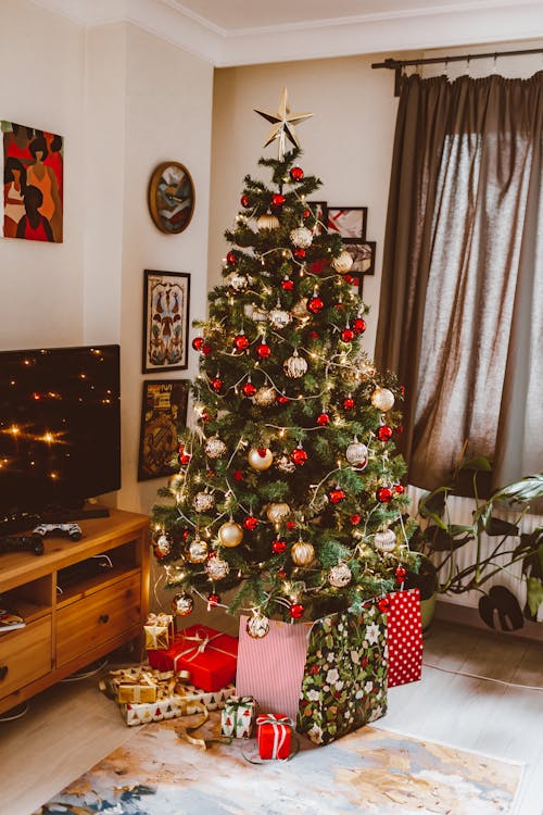 Free Elegant Christmas tree with ornaments in a modern living room setting, perfect for holiday festivities. Stock Photo