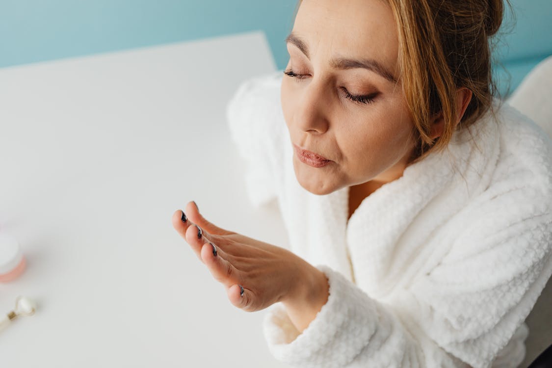 Free Woman in a bathrobe blowing on freshly painted nails, focusing on self-care and relaxation indoors. Stock Photo