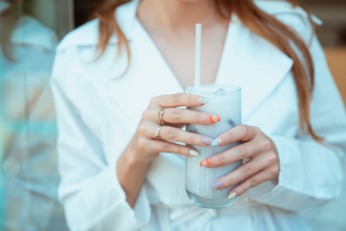 Free A stylish woman with colorful nails holds an iced drink in a cafe setting. Stock Photo