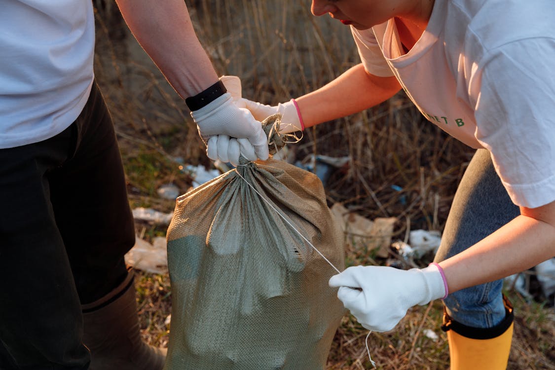 Free Two people tying a sack of garbage during an outdoor community cleanup activity. Stock Photo