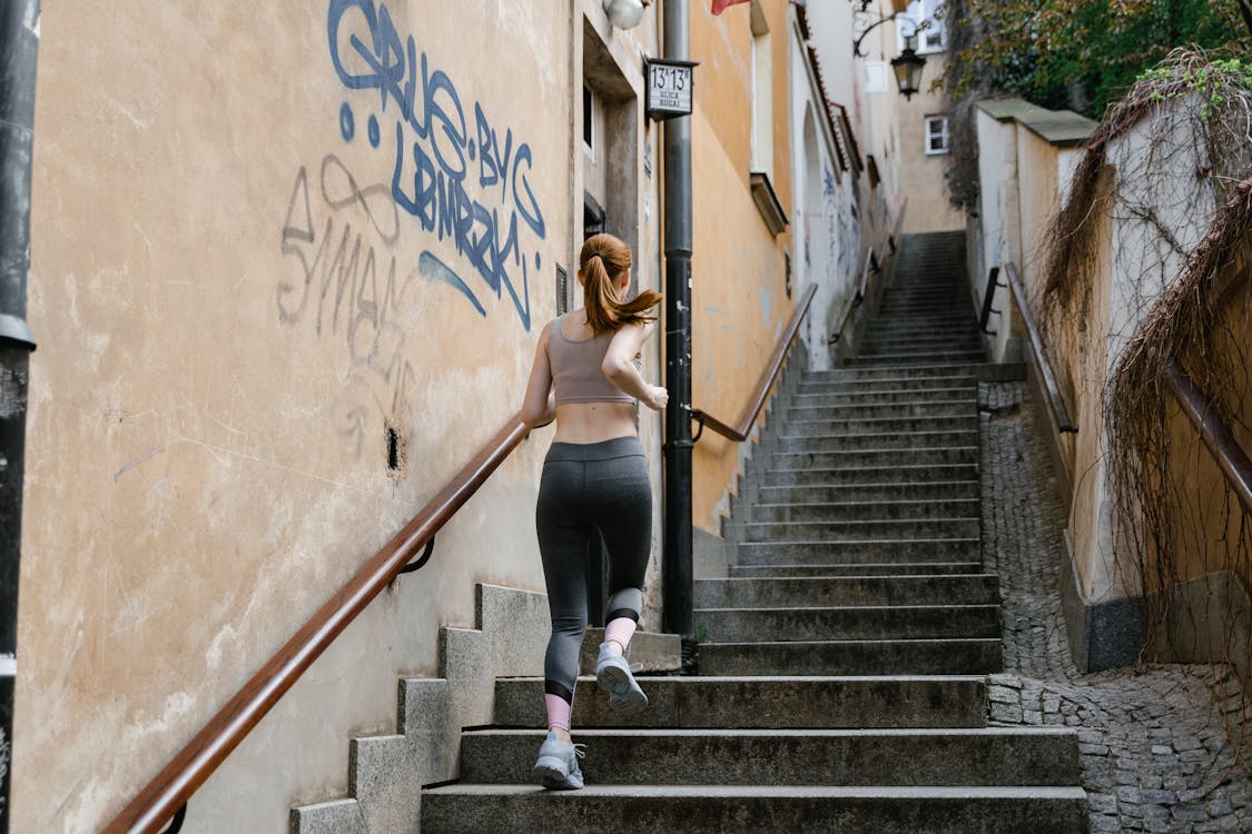 Free Back view of a female runner exercising on outdoor stairs in an urban setting. Stock Photo