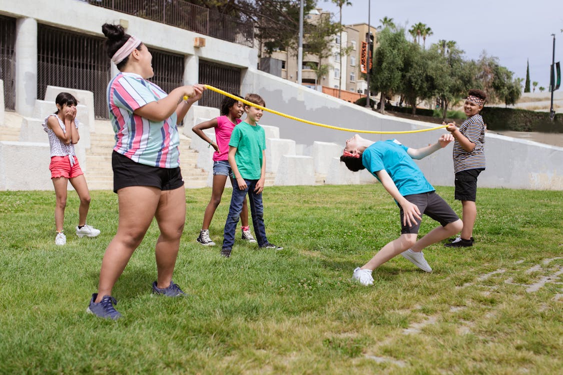 Free A group of children playing limbo outdoors during a fun summer camp activity on green grass. Stock Photo