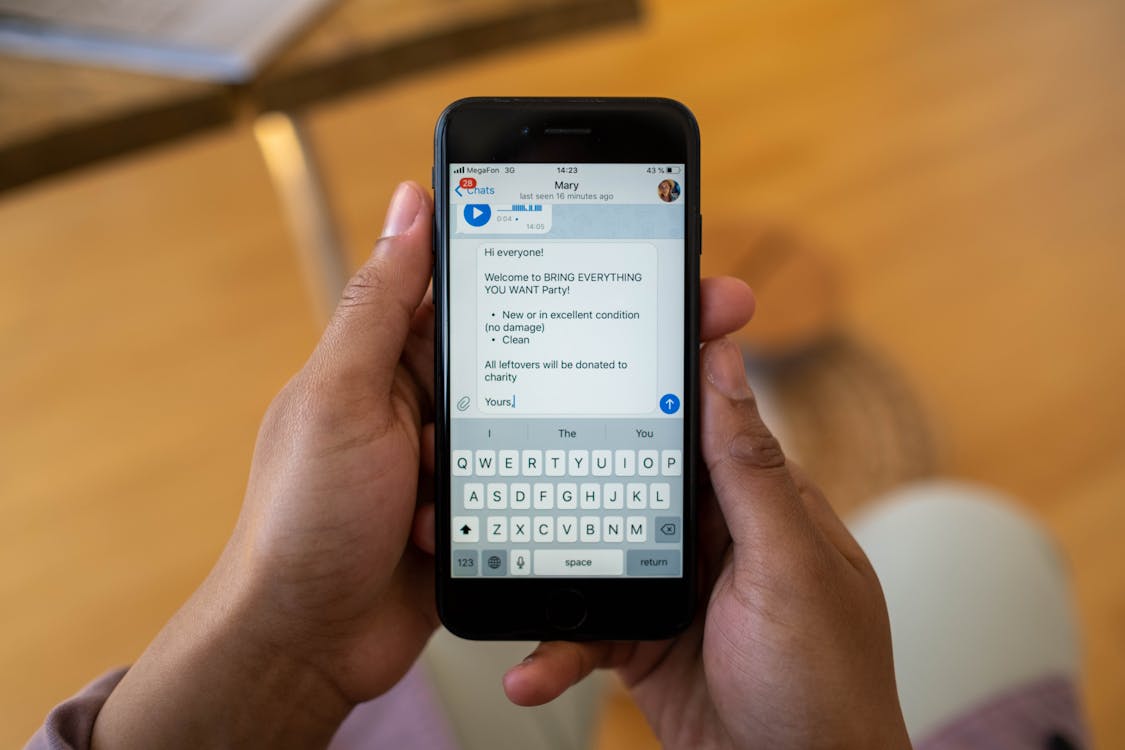 Free Person holding a smartphone displaying a text message about a party event indoors. Stock Photo