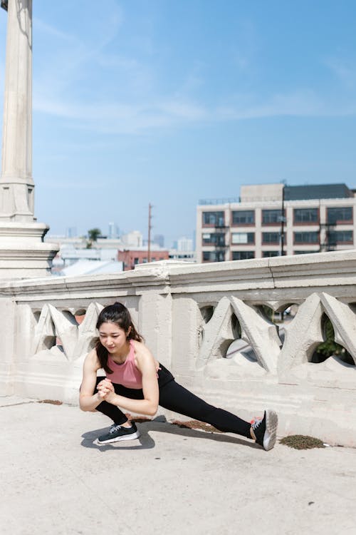 Free Young woman in activewear performing a stretch outdoors on a sunny day. Stock Photo