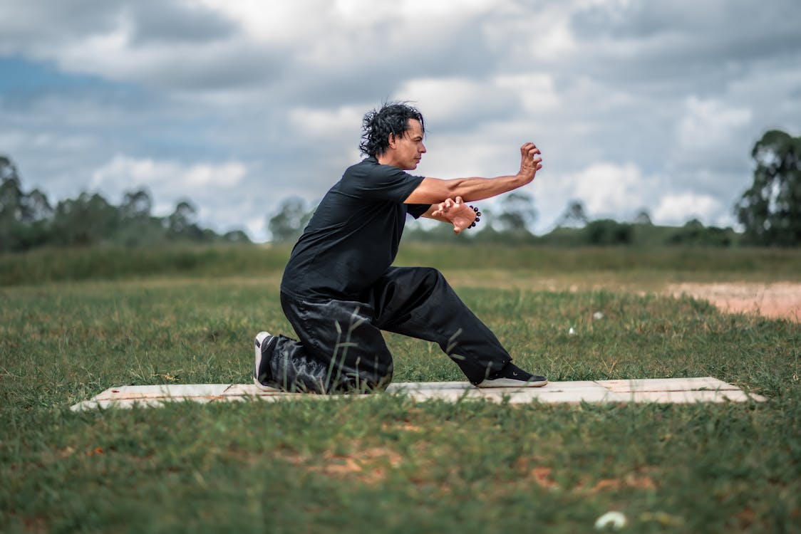 Free Man in black practicing Tai Chi in a grassy field outdoors, focusing on mindfulness. Stock Photo