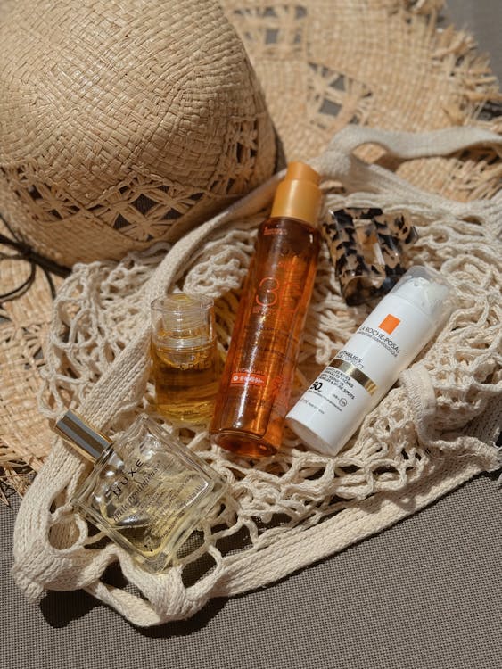 Free Stylish flat lay of beach bag essentials including a straw hat, sunscreen, and perfume for summer relaxation. Stock Photo