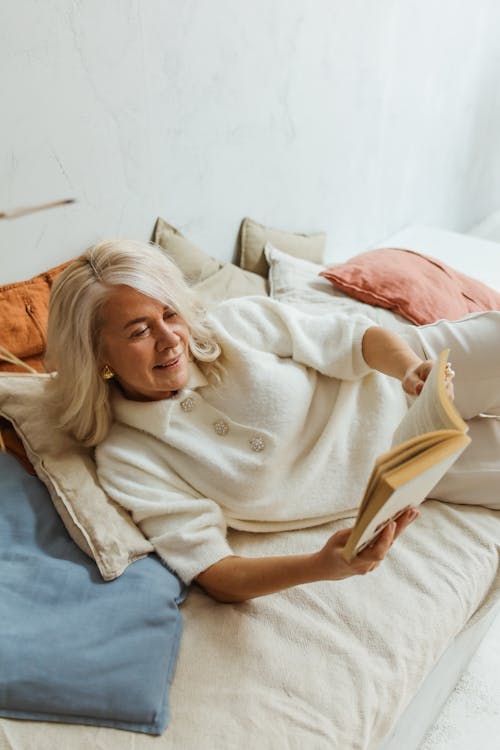 Free Elderly woman in a cozy setting enjoying leisure reading while lying on a bed. Stock Photo