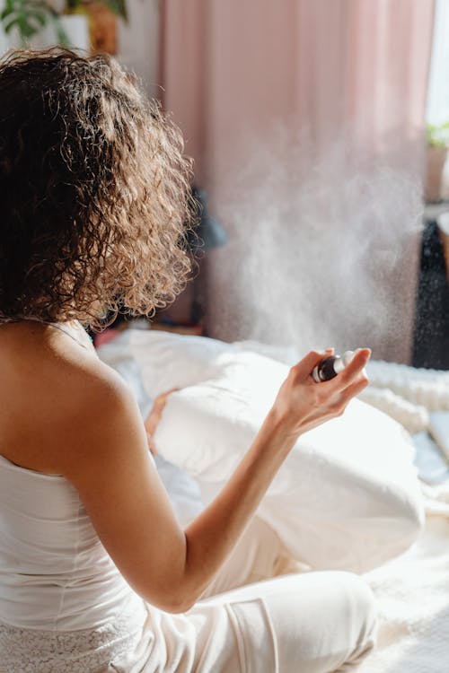 Free A woman in a cozy indoor setting using an aromatherapy spray on her pillow for relaxation. Stock Photo