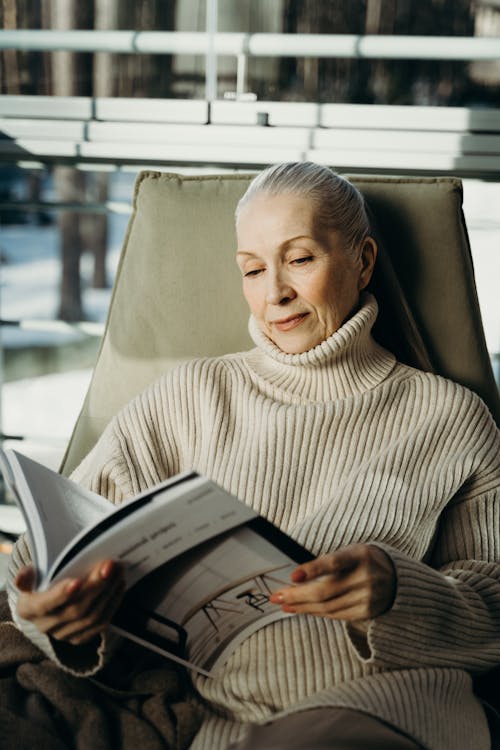 Free Senior woman enjoying a peaceful moment reading a magazine indoors. Stock Photo