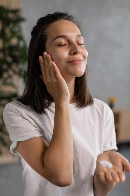 Free A woman enjoying her skincare routine, applying cream with a smile, indoors. Stock Photo