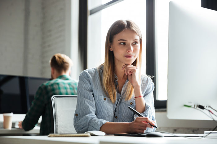 Young female engineer working at computer, thoughtfully planning software access and learning for HR team support.