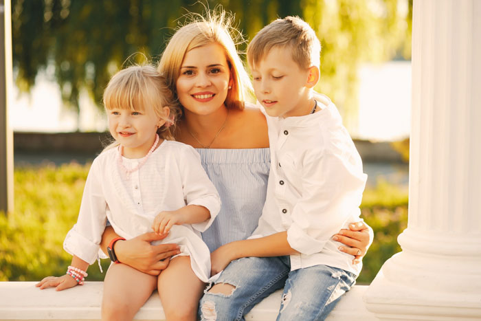 Mom with two children outdoors in sunlight, illustrating family care and challenges with disabled daughter responsibilities.