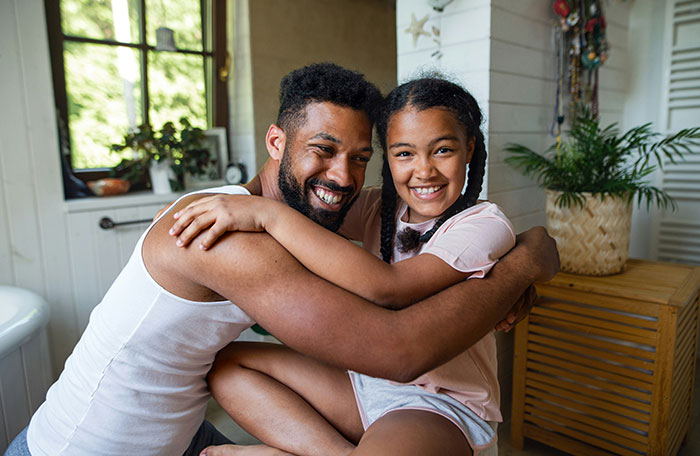 Father and daughter smiling and hugging indoors, illustrating clueless dad and period swimming paper towel discussion.