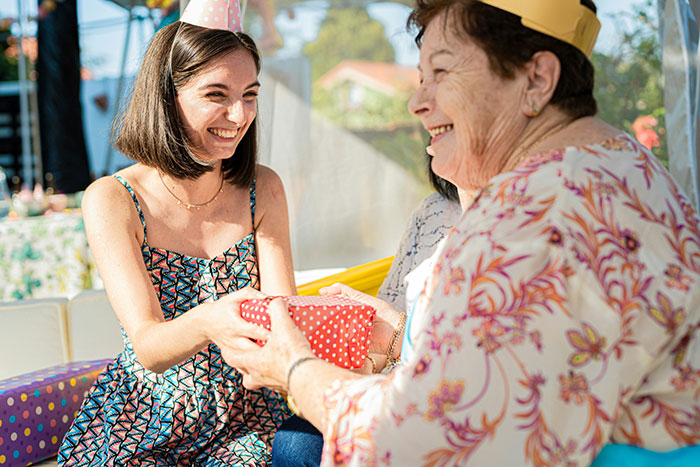 Teen girl in patterned dress smiling while receiving a gift from older woman at a shared birthday celebration.