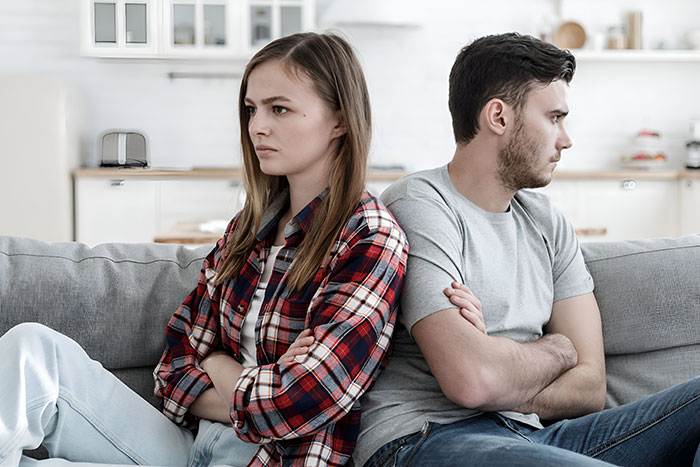 Young woman suggests an open relationship while the guy immediately breaks up, both sitting back-to-back looking upset.